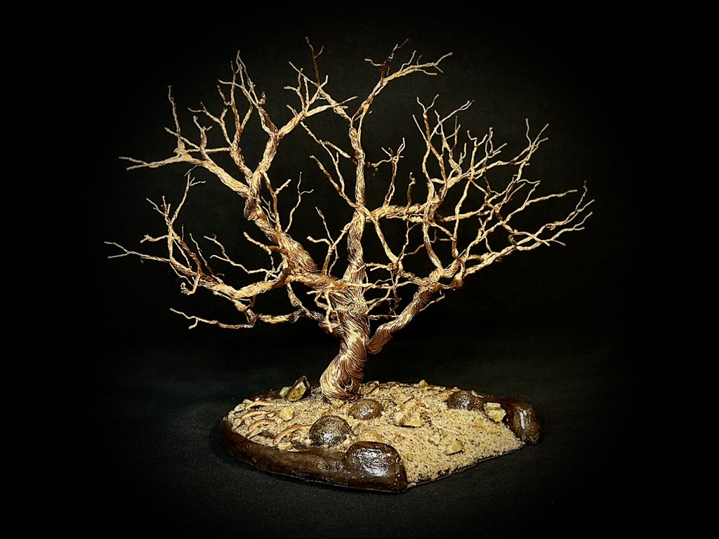 Branching copper wire tree sculpture on a sandy natural base against black
