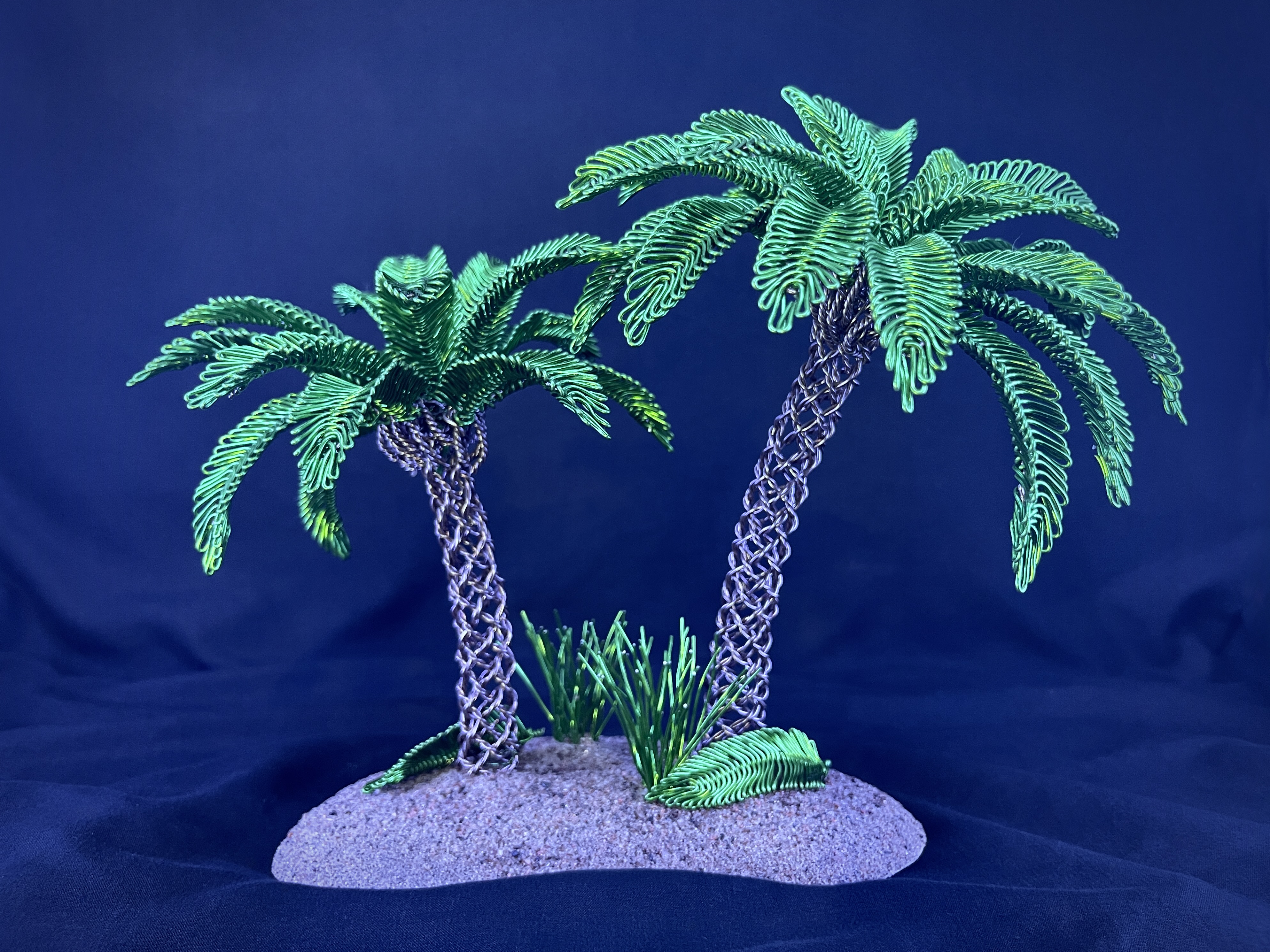 Pair of green wire palm trees rooted on a sandy island base against deep blue