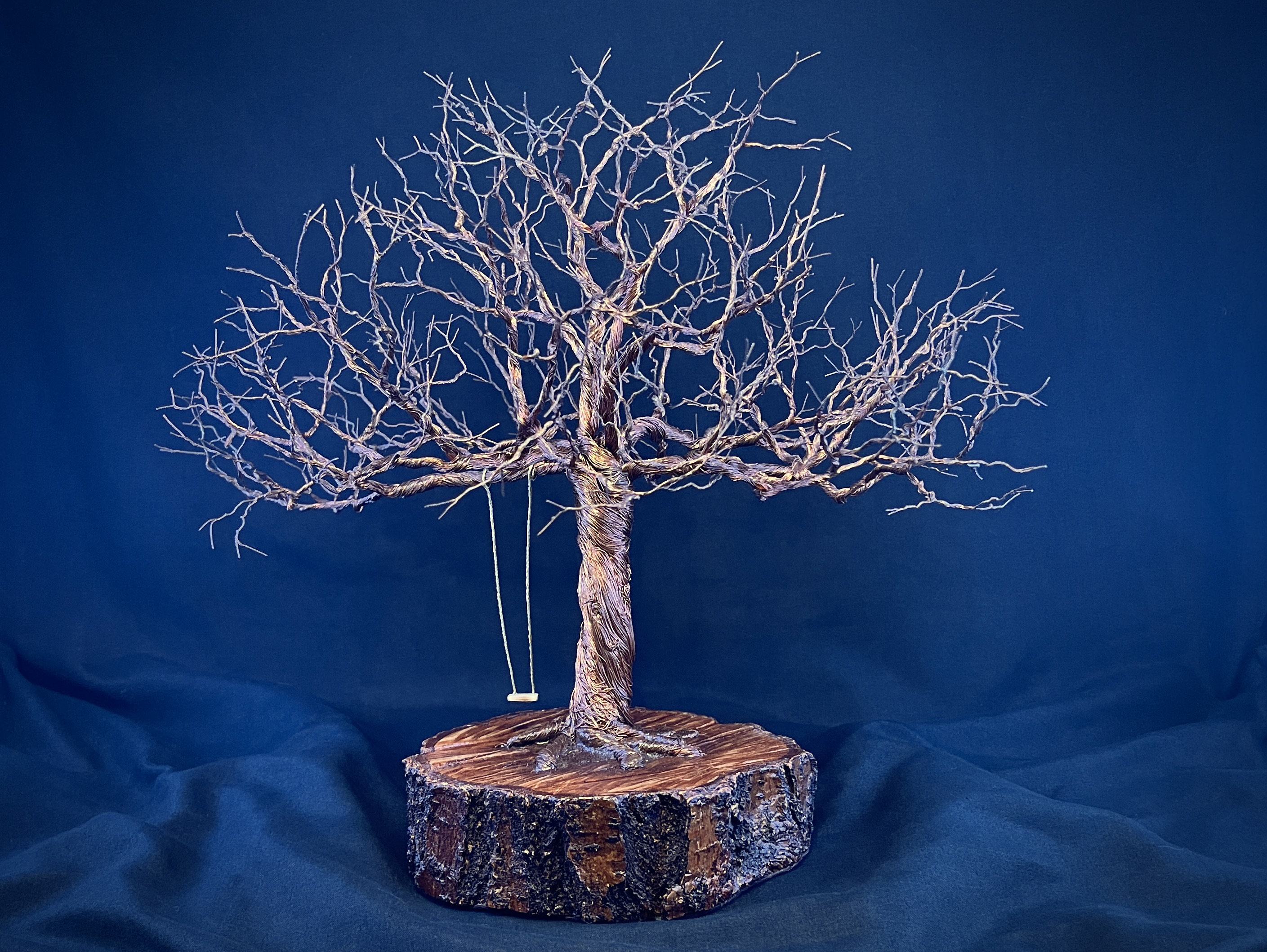 Broad copper wire tree sculpture on a natural wood slice against deep blue