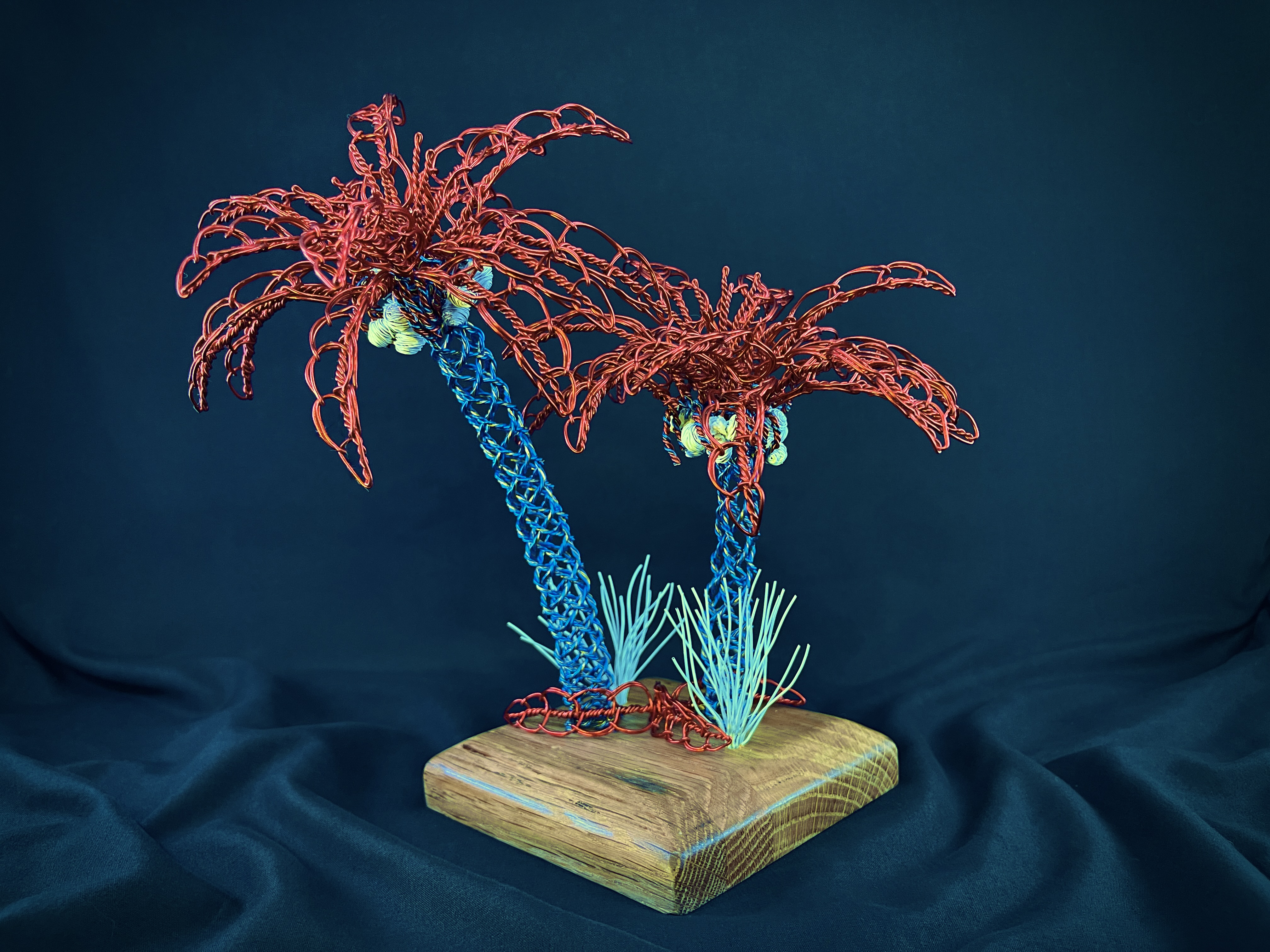 Pair of red and blue wire palm trees on a wood base against deep blue
