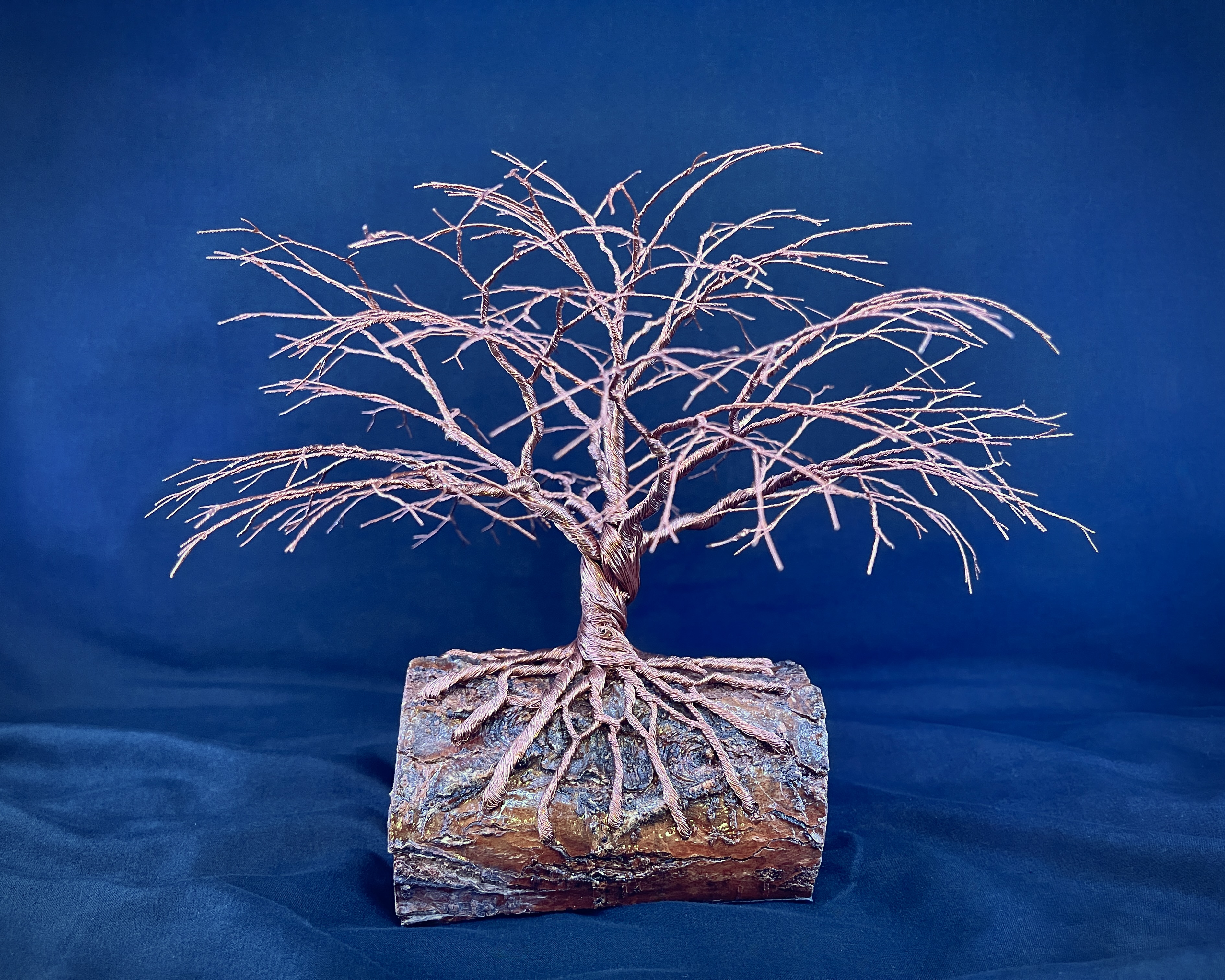 Full copper wire tree sculpture with exposed roots on a natural log base against deep blue