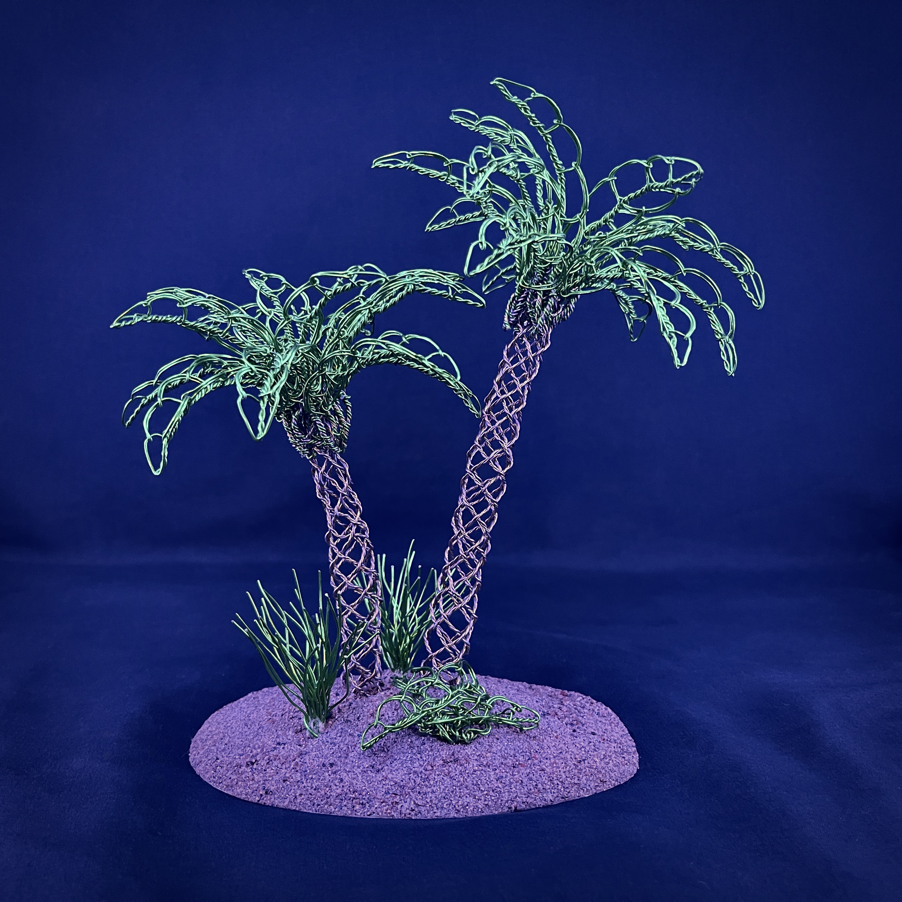 Pair of green wire palm trees sculpted on a sandy island base against black